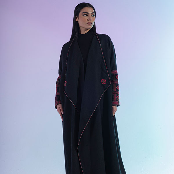 A hand-embroidered wool abaya with red threads and patterns inspired by the Najd region